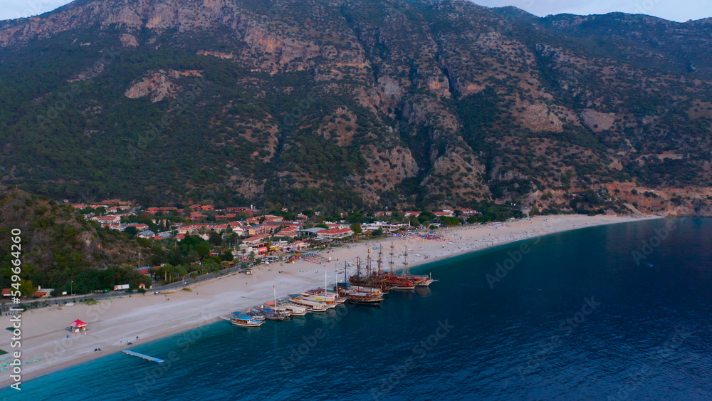 Aerial panoramic view from drone of coastal town and mountains. Yachts and boats parked on the beach of resort town.