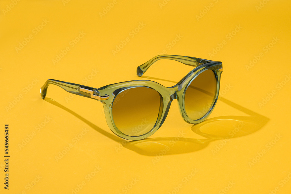 Female sunglass in sunlight on summer pastel yellow background. Women stylish eyeglasses for banner. Transparent plastic glasses. Female sunglass in sunlight on summer pastel yellow background. Women stylish eyeglasses for banner. Transparent plastic glasses.
