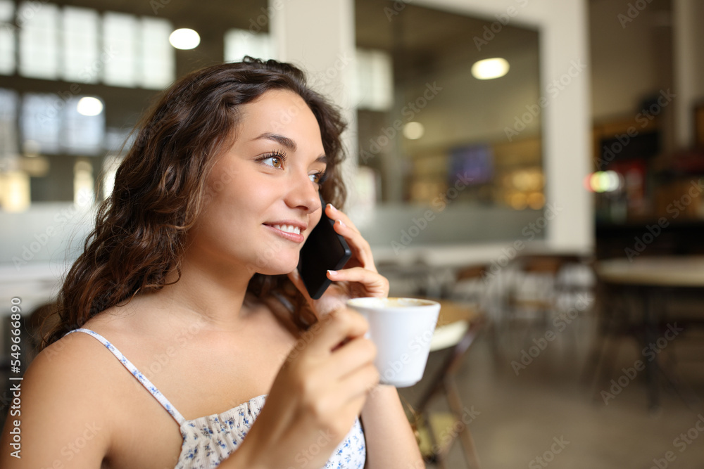 Happy woman drinking coffee talking on phone in a bar Happy woman drinking coffee talking on phone in a bar