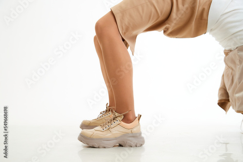 Beautiful sneakers on woman legs in the studio on white background. Fashionable shooting of a young girl with beautiful legs