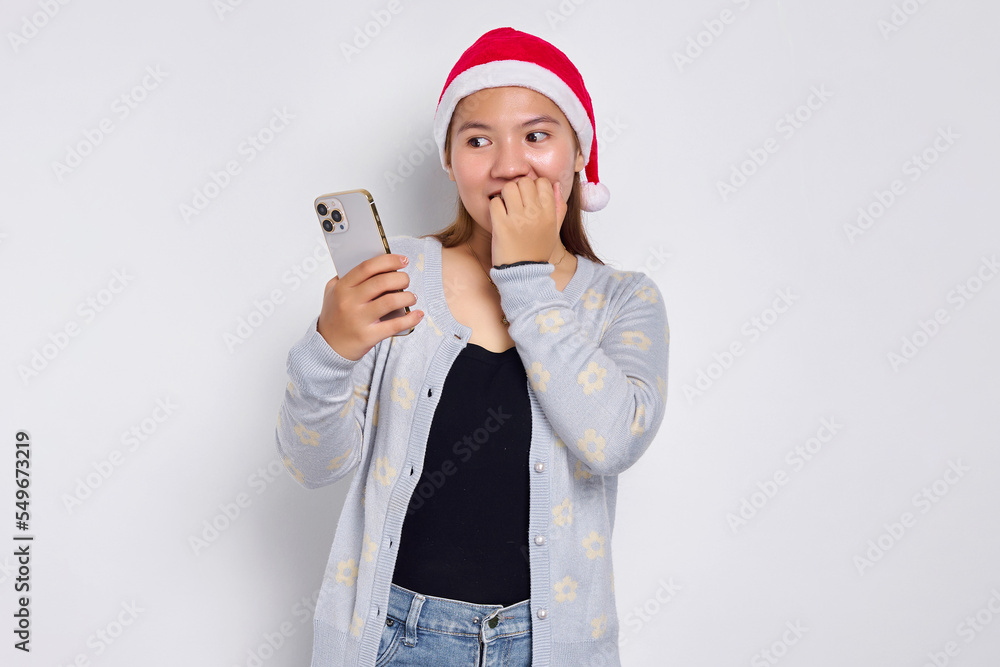 Anxious young Asian woman in a Christmas hat using mobile with worried expression isolated over white background Anxious young Asian woman in a Christmas hat using mobile with worried expression isolated over white background