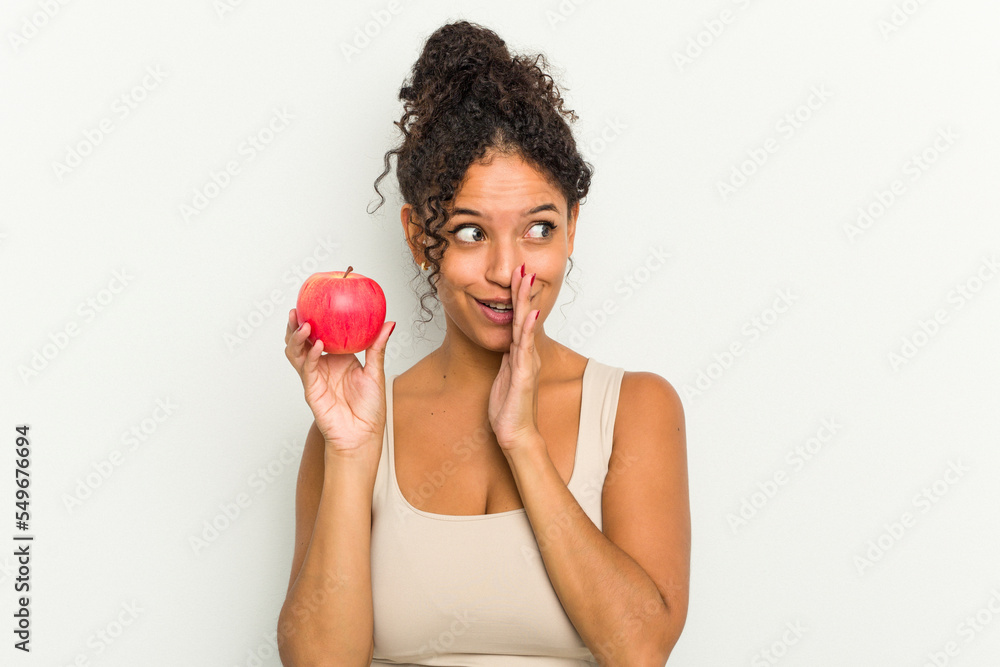 Young brazilian woman holding a red apple isolated is saying a secret hot braking news and looking aside Young brazilian woman holding a red apple isolated is saying a secret hot braking news and looking aside