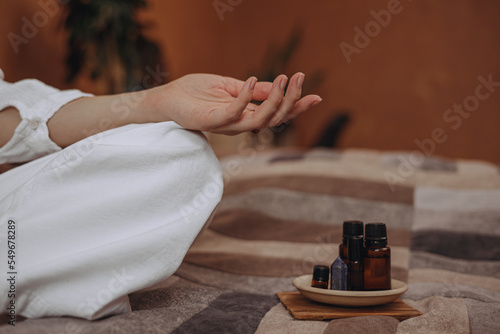 Crop woman with mudra hand doing yoga on bed with essential oils for aromatherapy at home 