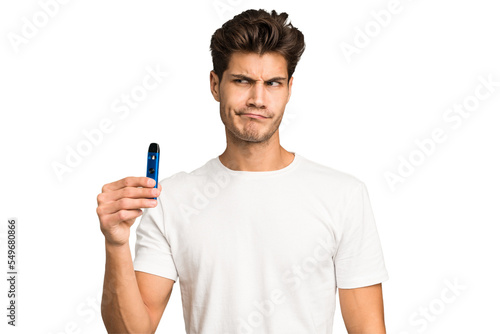 Young caucasian man holding an electronic cigarette isolated confused, feels doubtful and unsure.