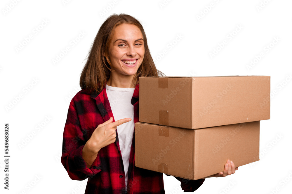 Young caucasian woman moving while picking up a box full of things isolated smiling and pointing aside, showing something at blank space. Young caucasian woman moving while picking up a box full of things isolated smiling and pointing aside, showing something at blank space.