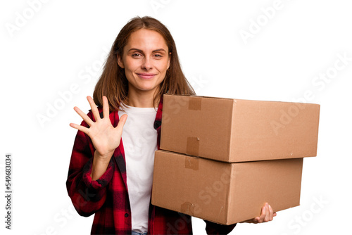 Young caucasian woman moving while picking up a box full of things isolated smiling cheerful showing number five with fingers.