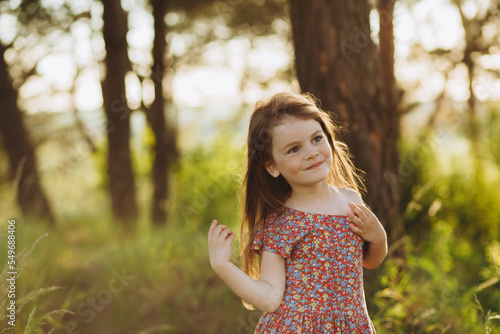 Little girl wearing pink dress taking a walk all alone in a park or forest