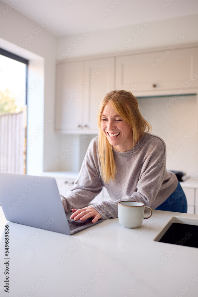Woman At Home Working On Laptop On Counter In Kitchen Woman At Home Working On Laptop On Counter In Kitchen