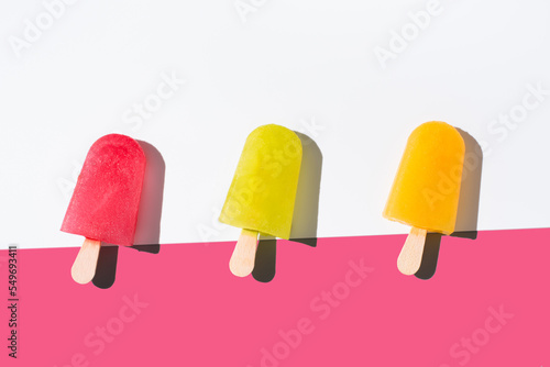 Paletas de hielo de colores. Palitos de helado naranja, rojo y amarillo sobre fondo rosa y blanco. Concepto de verano. Vista superior	