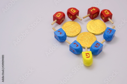 Multicolor Heart dreidels and chocolate golden coins. Hanukkah and judaic holiday concept. Copy space on white background. Family game for the holiday of Light and love. Postcard and place for text photo