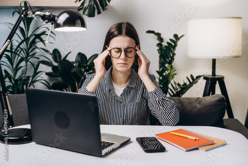 Tired young woman in eyeglasses with laptop sit on sofa suffer migraine. Sad female suffers from dry irritable eyes after long notebook usage. Eye strain, conjunctivitis infection need drops concept