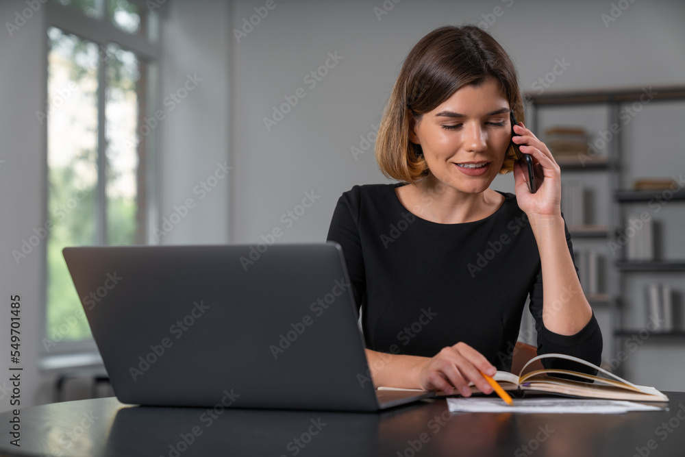 Smiling businesswoman in formal wear talking on smartphone taking notes Smiling businesswoman in formal wear talking on smartphone taking notes