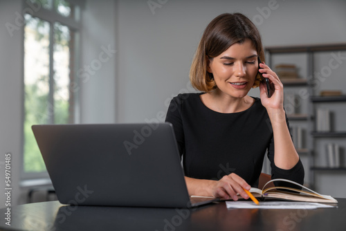 Smiling businesswoman in formal wear talking on smartphone taking notes