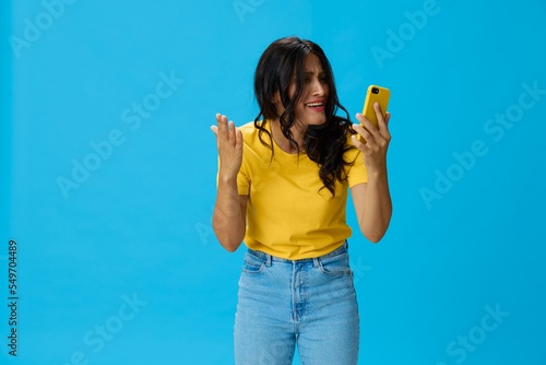 Woman with a phone in her hands with a yellow case on a blue background in a yellow T-shirt, emotions signals gestures, online lifestyle concept, shopping, communication, learning, business online