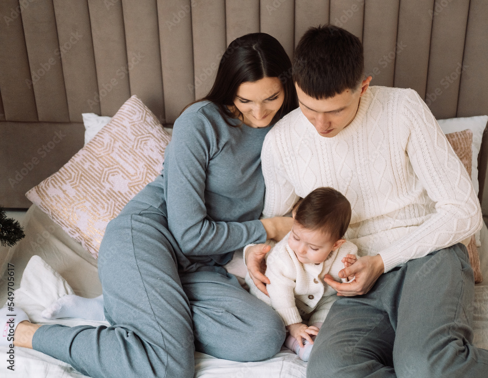 Young family with a baby, lie on the bed, have fun. Concept of childhood, love and family.