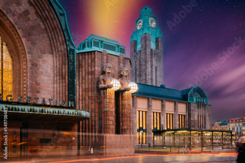 Helsinki, Finland. Very Peri Starry Sky Above Statues On Entrance To Helsinki Central Railway Station. Evening Or Night Illumination. Light Violet Colors. Bright Dramatic Yellow Light Purple Sky.