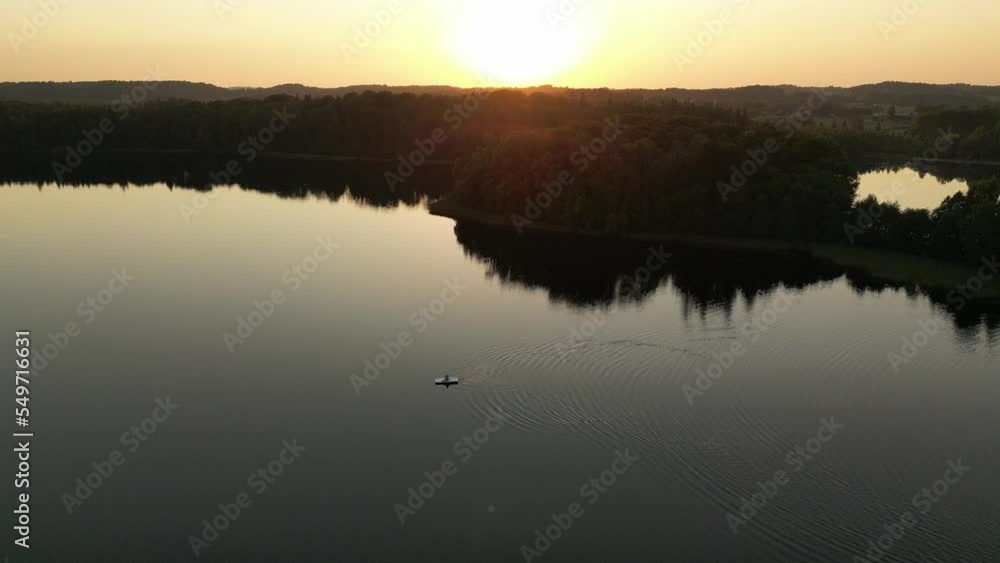 Drone view of a boat on a lake enjoying sunset. Sun settling behind the green forest. Movement on the water top view. Ocean sea water wave reflections. Lonely boat alone in the lake. Drone view of a boat on a lake enjoying sunset. Sun settling behind the green forest. Movement on the water top view. Ocean sea water wave reflections. Lonely boat alone in the lake.