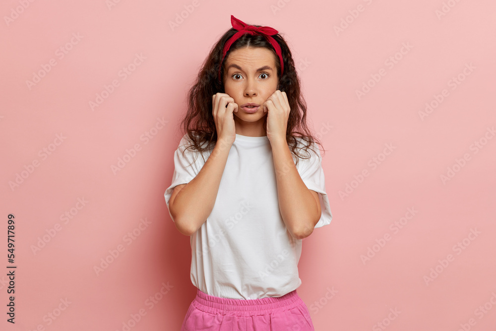 Woman shows scare emotion, stands isolated over pink, keeps arms close to her face Woman shows scare emotion, stands isolated over pink, keeps arms close to her face