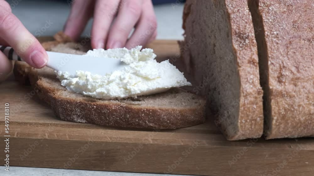 Women's hands smear bread with cream cheese on a wooden board. Cooking breakfast concept. Women's hands smear bread with cream cheese on a wooden board. Cooking breakfast concept.