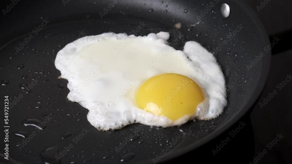 Frying egg in black frying pan. Breakfast preparation process. Frying egg in black frying pan. Breakfast preparation process.