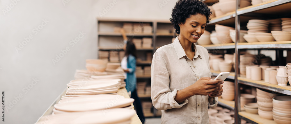 © (JLco) Julia Amaral - Smiling ceramist using a smartphone in her shop