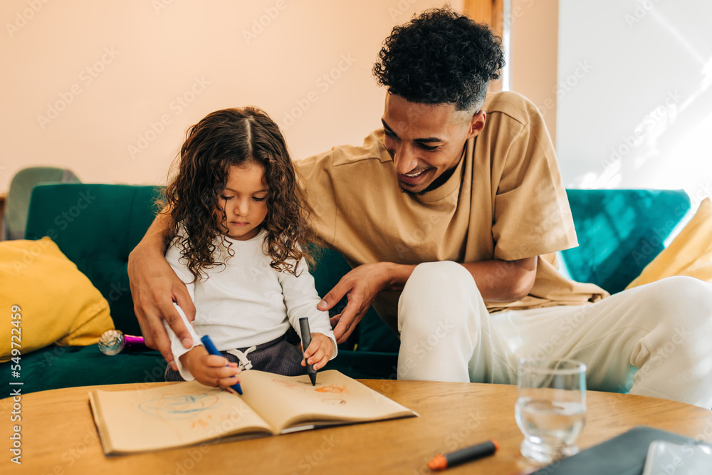 Cheerful single father teaching his daughter how to draw in a colouring book Cheerful single father teaching his daughter how to draw in a colouring book
