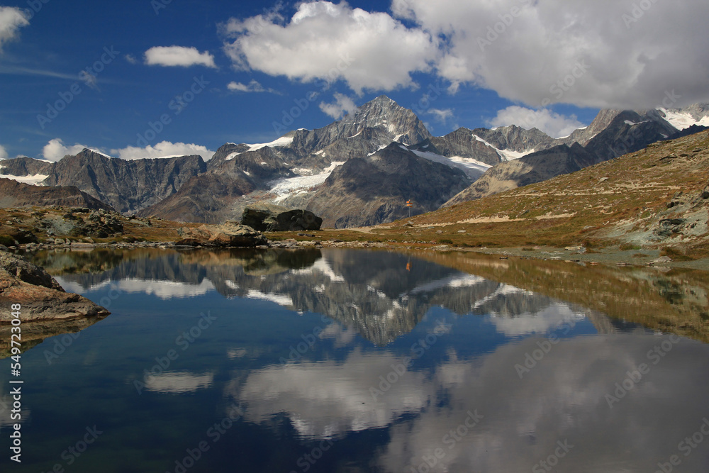 A landscape with a smooth Riffelsee lake surface and mountains and clouds reflected in it, on a mountain Gornergrat, near Zermatt, in southern Switzerland