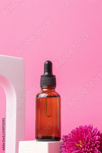 Serum with floral extracts for skincare in arch. Nature cosmetics in glass bottle with pipette and pink flowers on pink background. Face and body care spa concept.