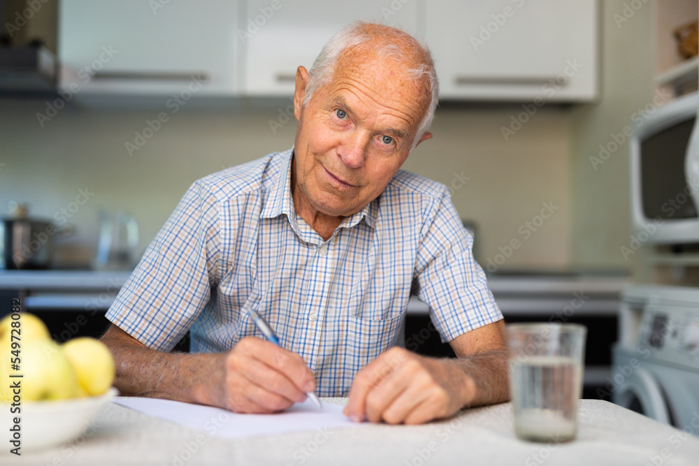Fototapeta premium Man writing letter on paper while sitting in kitchen at home