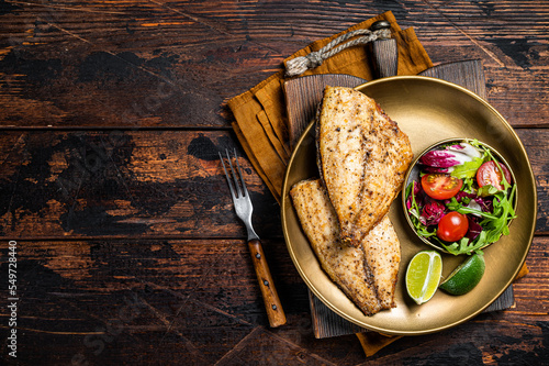 Roasted Gilthead Sea Bream fillets served with fresh vegetable salad. Wooden background. Top view. Copy space