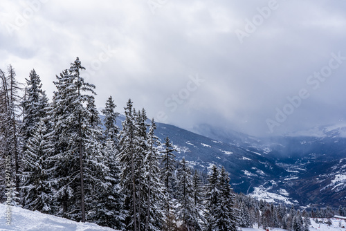 View from the distance to the ski resort. Mountain valley with spruce trees, clody sky. Beautifull panoramic view from the top of the mountain in french alps.