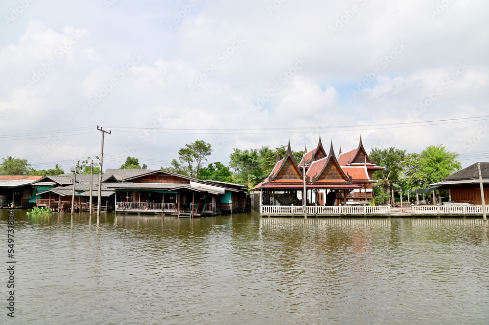BANGKOK, THAILAND - NOVEMBER 20, 2022 : Wooden houses, Thai houses and buildings along the Chao Phraya River with white clouds and blue sky background, Town Ayutthaya Waterfront, Thailand. BANGKOK, THAILAND - NOVEMBER 20, 2022 : Wooden houses, Thai houses and buildings along the Chao Phraya River with white clouds and blue sky background, Town Ayutthaya Waterfront, Thailand.