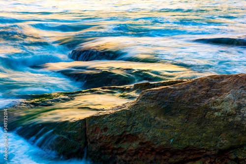 Sea water blurred by the movement and dripping between the stones with the colors and brightness of the sunset on Ipanema beach in Rio de Janeiro © Fred Pinheiro