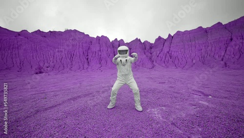 A cheerful astronaut dances on a purple planet. The astronaut is very happy about his trip to a distant planet and dances on it joyfully.