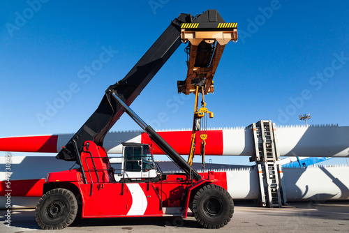 Φωτογραφία A four-wheeled mobile container loader parked at the seaport, next to the storage blades for wind turbines