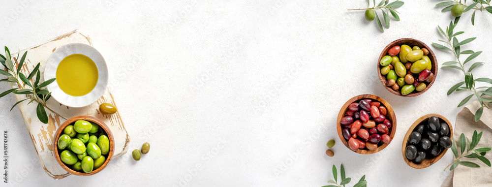 Different olives in bowls on white concrete background. Top view of olives, olive leaves and bottle of olive oil. Diet food concept. Banner. Different olives in bowls on white concrete background. Top view of olives, olive leaves and bottle of olive oil. Diet food concept. Banner.