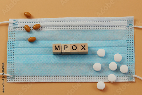 Mpox is laid out with wooden cubes on a surgical face mask. There are various pills lying around. MPOX is the new name for the monkeypox virus.  photo