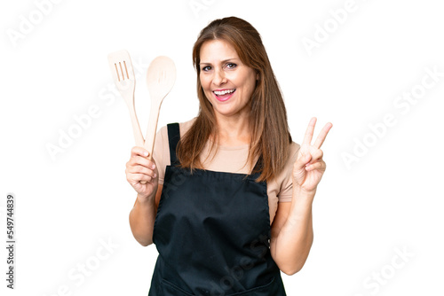 Middle age caucasian woman holding a rolling pin over isolated background smiling and showing victory sign