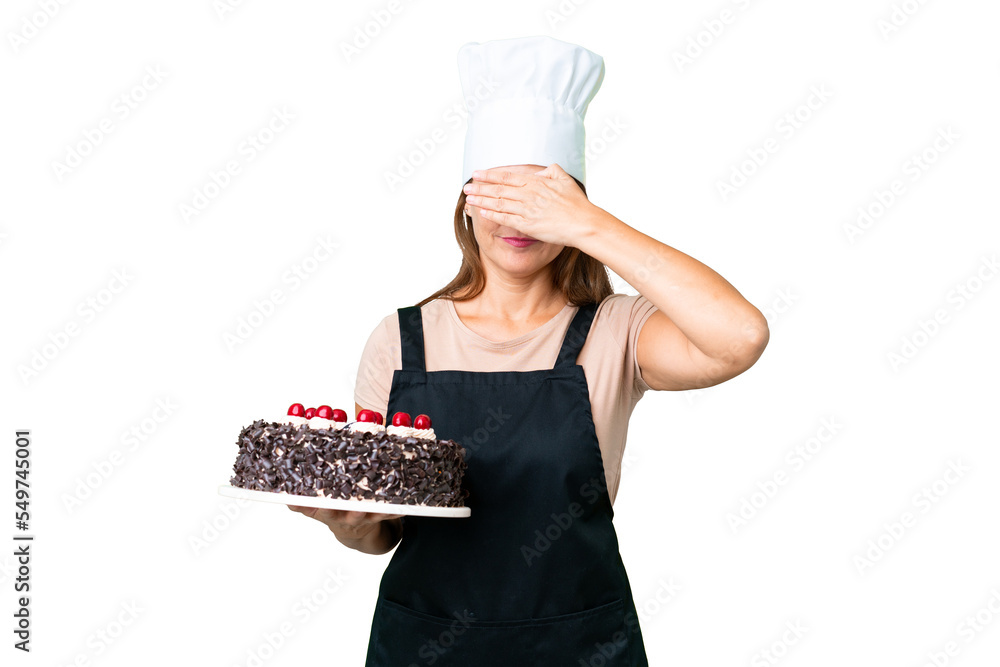 Middle age pastry chef woman holding a big cake over isolated background covering eyes by hands. Do not want to see something Middle age pastry chef woman holding a big cake over isolated background covering eyes by hands. Do not want to see something