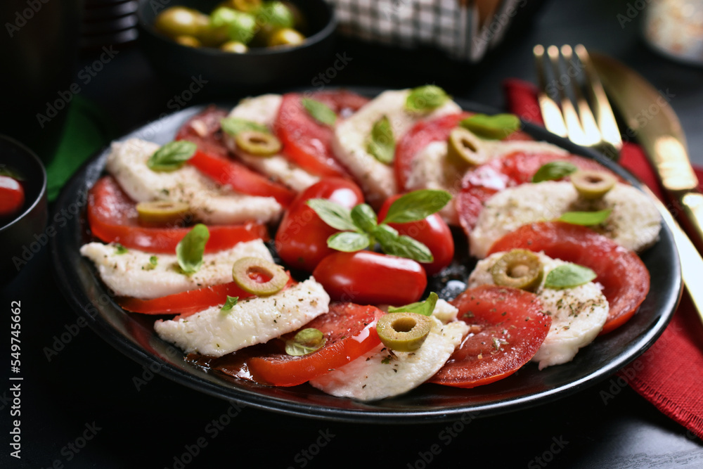 Caprese salad with mozzarella and tomatoes on black plate and table Caprese salad with mozzarella and tomatoes on black plate and table