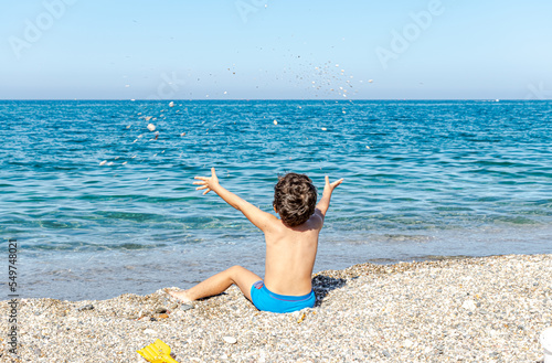 Bild auf Leinwand Unrecognizable little child sitting on the puddle beach shore with open arms thr