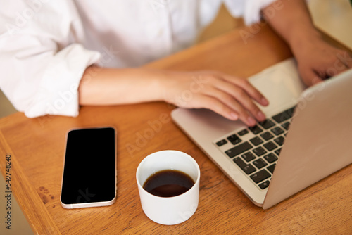 Cropped shot of female hands typing on laptop keyboard, drinking coffee, working in cafe, studying, doing homework photo