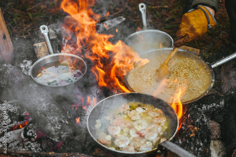 A large pan of shrimp in is cooked above an open flame set in an outdoor A large pan of shrimp in is cooked above an open flame set in an outdoor