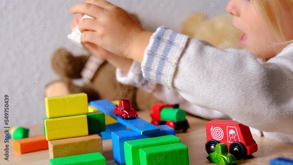 small child, blonde girl 3 years old plays toys, builds towers and buildings from colored wooden figures, concept of housing construction, insurance, happy childhood, children's games, selective focus small child, blonde girl 3 years old plays toys, builds towers and buildings from colored wooden figures, concept of housing construction, insurance, happy childhood, children's games, selective focus