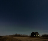 Stary dark blue night sky above an abandoned farmhouse next to a gravel road.
