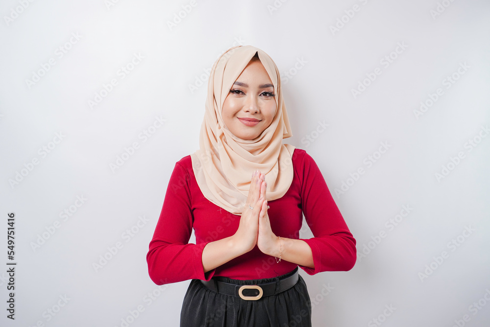 Fototapeta premium Portrait of a young beautiful Muslim woman wearing a hijab gesturing Eid Mubarak greeting