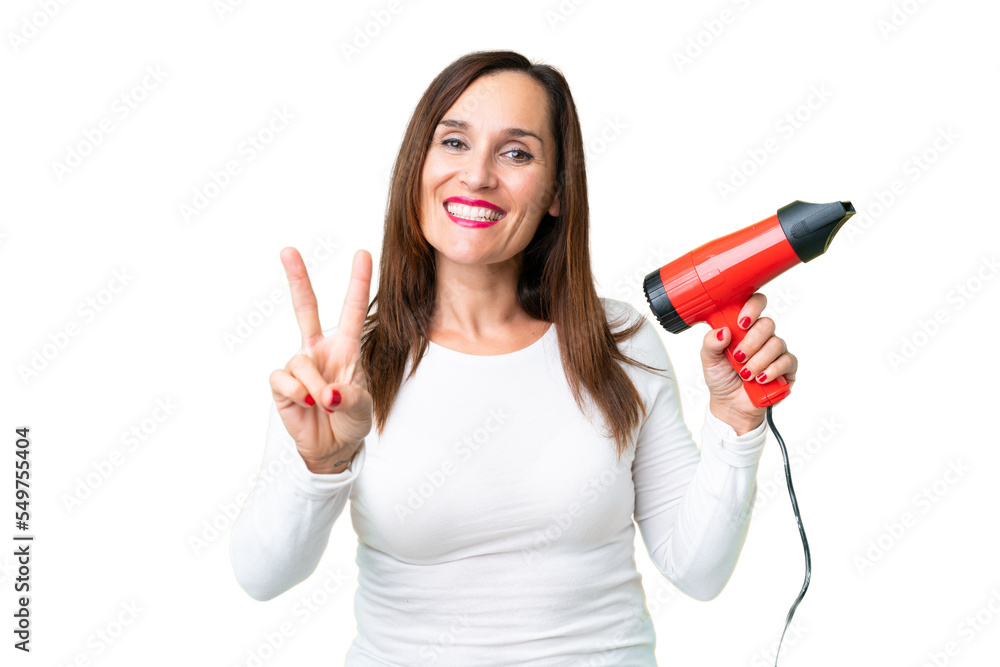 Middle age woman holding a hairdryer over isolated chroma key background smiling and showing victory sign Middle age woman holding a hairdryer over isolated chroma key background smiling and showing victory sign