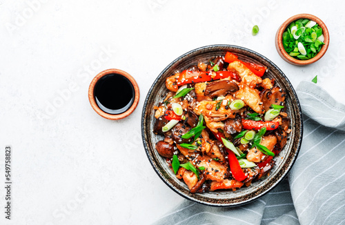Stir fry with turkey fillet, red paprika, mushrooms, green chives and sesame seeds in bowl Asian cuisine dish. White kitchen table background, top view