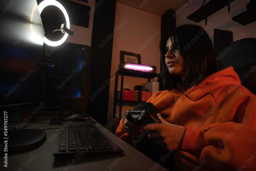 the gamer girl in the orange sweatshirt plays video games on her computer in her set-up. the gamer girl in the orange sweatshirt plays video games on her computer in her set-up.