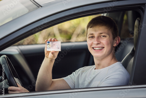 Happy and proud guy showing his driver license out of the car window